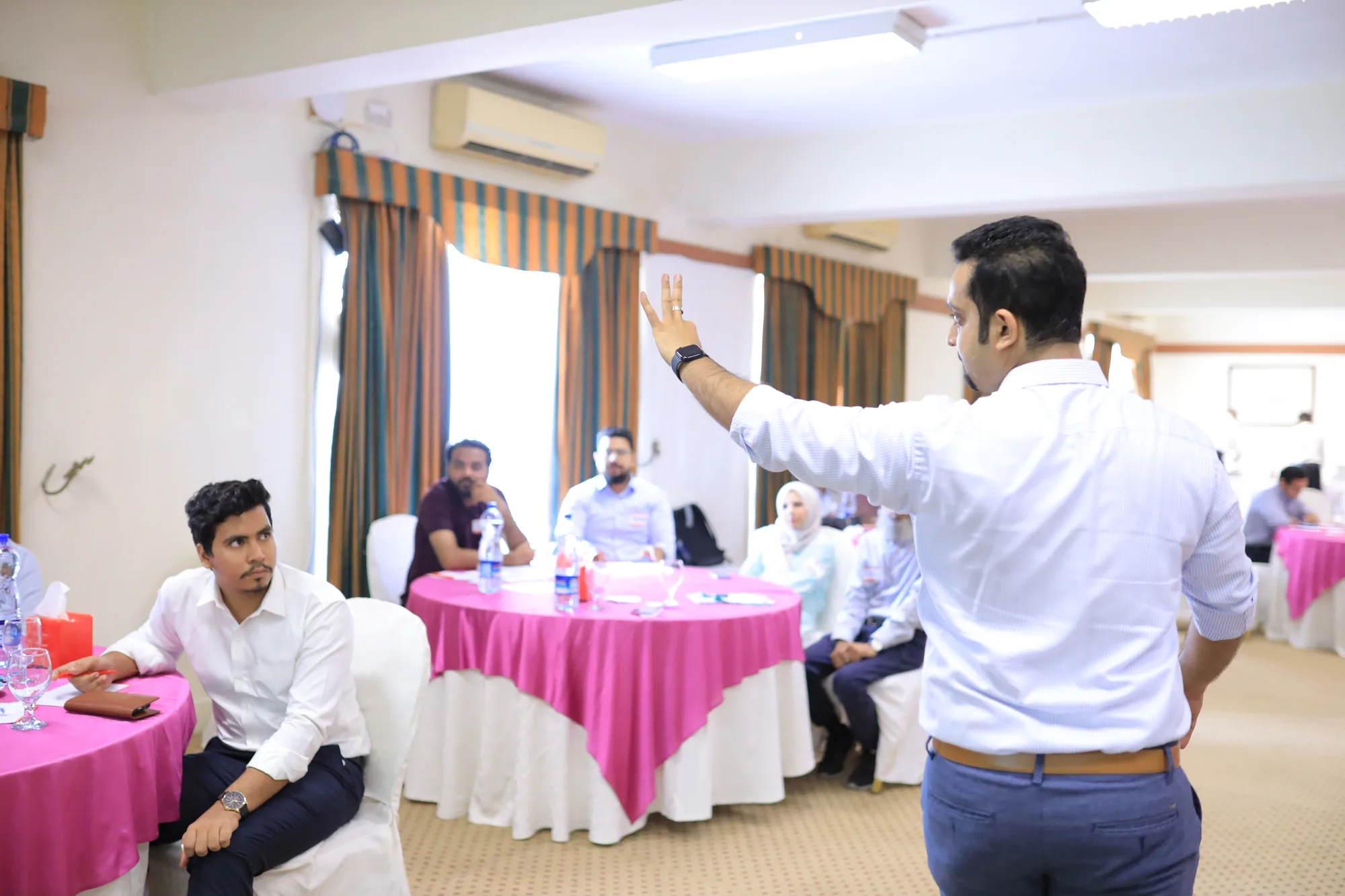 Zain Goplani facilitating an experiential learning session with participants seated at round tables
