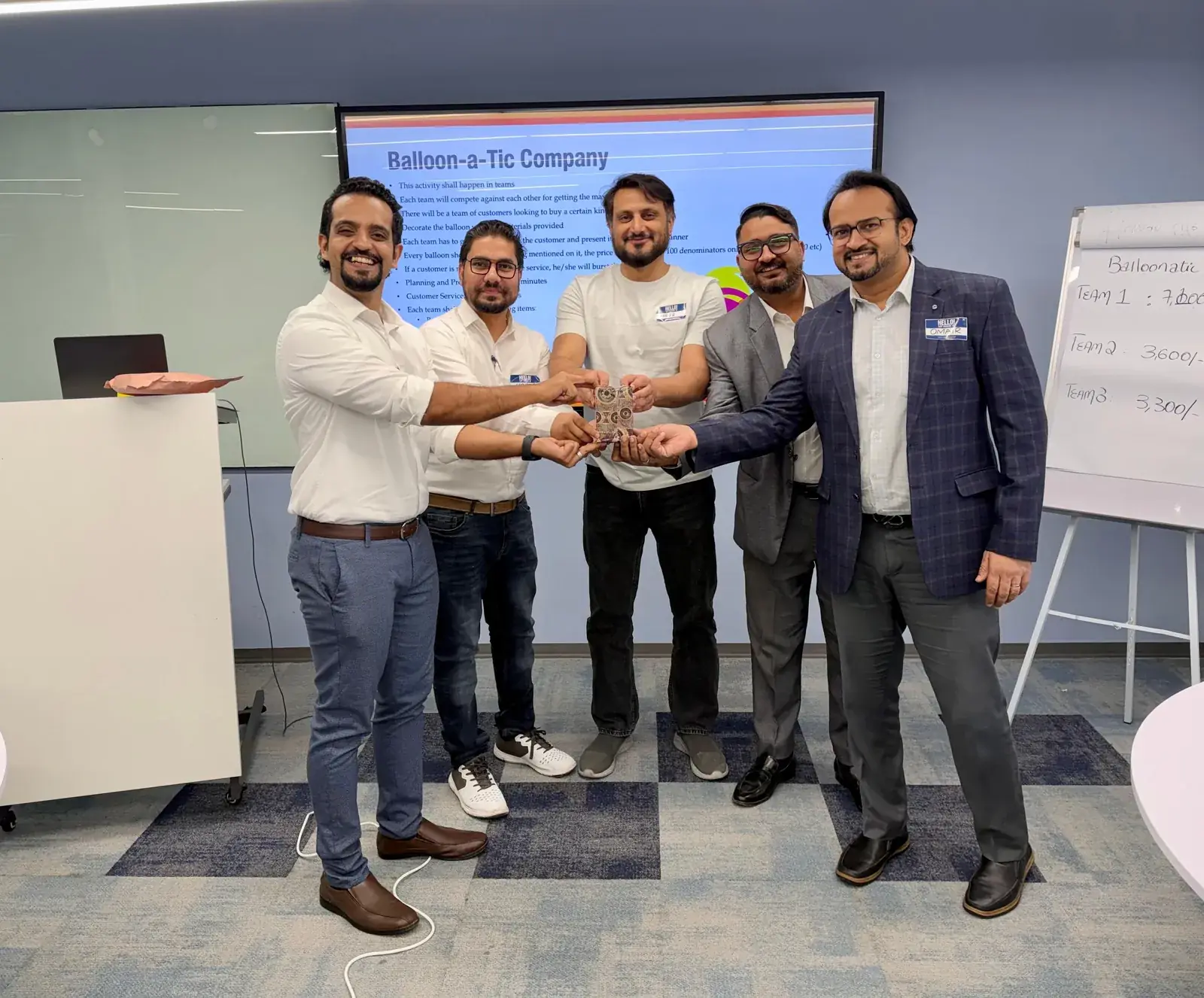 Winning team holding their award after a team-based sales simulation, with the activity brief and team scores in the background